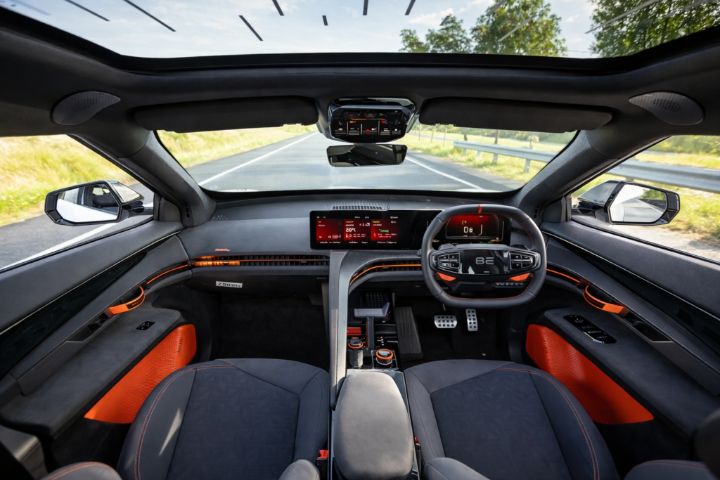 Mahindra BE 6 electric SUV interior with dual digital screens, sporty steering wheel, panoramic sunroof, and black-orange premium cabin design.