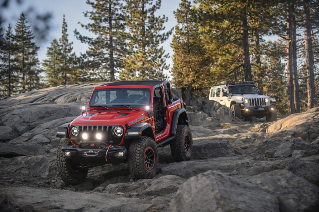 “Pathrile jungle off-road trail par chalti hui laal Jeep Rubicon, aage rocky terrain par, peeche safed Jeep aur ghane ped.”