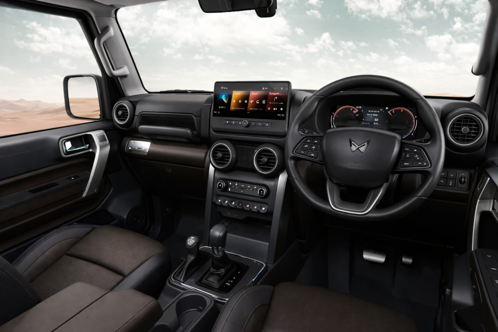 “Mahindra Thar ROXX ka interior view, right-hand drive layout ke saath, black dashboard, multifunction steering wheel, digital instrument cluster, touchscreen infotainment system aur premium front seats; bahar desert landscape dikh raha hai.”